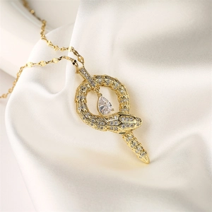 Macro shot of gold snake pendant with white crystals on a white silk background