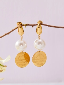Détail de boucles d'oreilles dorées vintage avec perle blanche et disque gravé sur branche