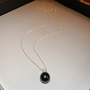 Detail of a minimalist gold necklace with a black pearl pendant and a sparkling zircon