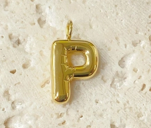 Macro shot of gold-plated P-shaped bubble letter charm on textured stone surface