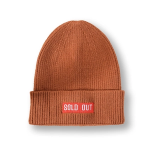 Gros plan sur un bonnet en tricot caramel avec un patch rouge 'SOLD OUT' sur le revers