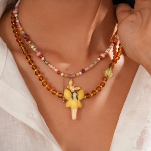 Close-up of double-layered beaded necklace with amber crystal and fairy charm