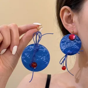 Detail of artistic royal blue round hoop earrings with woven knot and red bead accent
