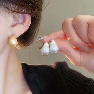 Detail showing matte gold and silver teardrop earrings with satin metal texture