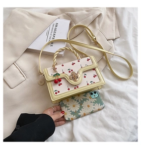 Detail of light yellow cherry print bag with a golden flower lock on beige fabric