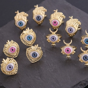 Detailed flat lay of 18K gold-plated eye rings in various colors on dark stone surface