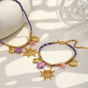 Détail de colliers en cordon tressé violet avec des pendentifs floraux plaqués or 18K