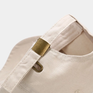 Detail of adjustable metal buckle and stitching on beige cotton skull baseball cap