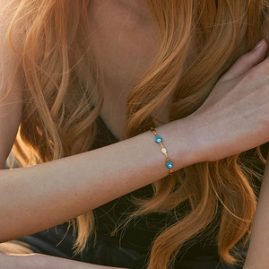 18K gold plated evil eye bracelet with blue Hamsa charms on a model wrist at sunset