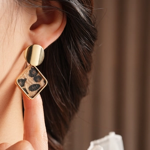 Gros plan de boucles d'oreilles dorées géométriques avec pendentifs léopard sur modèle