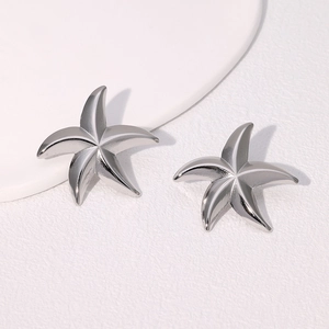 Macro shot of silver starfish stud earrings with glossy metallic finish on white texture