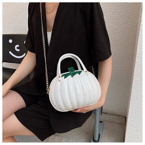 Close-up of shiny white pumpkin-shaped handbag with green leaf detail and gold chain