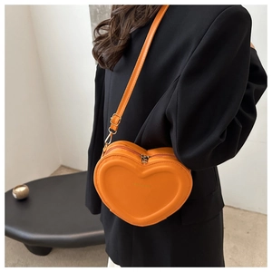 Close-up of heart-shaped crossbody bag in orange leather with embossed fashion logo
