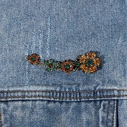 Detail of a floral brooch with orange rhinestones and green enamel on denim fabric