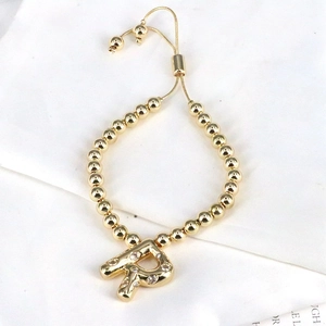 Close-up of gold beaded bracelet with zircon-encrusted letter A charm and adjustable cord