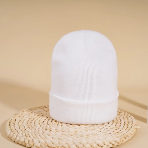 Close-up of white ribbed knit beanie with soft texture on a natural woven mat background