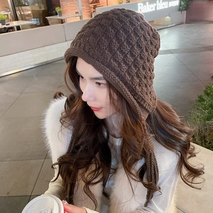 Detail of dark brown chunky knit beanie with braided tassels worn in a street setting
