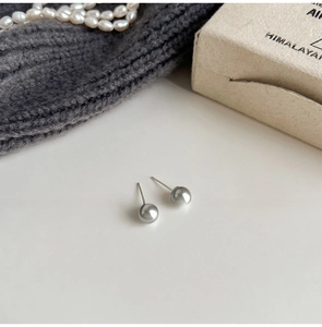 Detailed view of gray pearl stud earrings on a beige surface with soft lighting