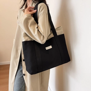 Black and beige canvas tote bag with wide shoulder strap on a model in trench coat