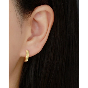 Close-up of golden round hoop earring with vertical stripes worn on a person