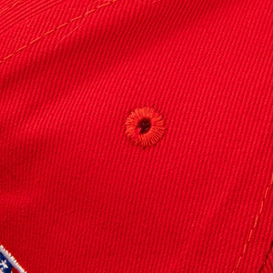 Close-up detail of red cotton twill fabric and embroidered eyelet on a baseball cap
