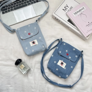 Detail van denim telefoontasje met sterrenpatroon, kattenpatch en rode knop op witte stof