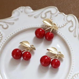 Detailed view of three red cherry pendants with gold leaves on a vintage ceramic plate