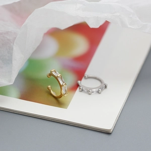 Detailed close-up of gold and silver ear cuffs with rectangular zircon on a magazine