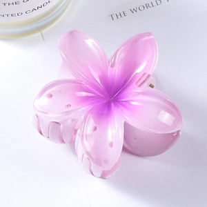 Pink and purple gradient plumeria flower hair claw clip on a minimalist white desk