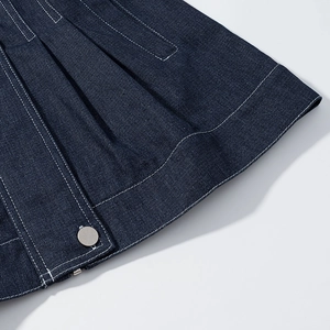 Detailed close-up of dark blue denim fabric with white stitching and silver metal button