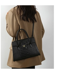 Detail of black crocodile texture handbag with gold twist lock on stylish camel blazer