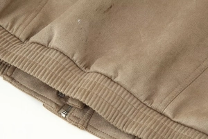 Close-up of brown suede jacket showing zipper detail and ribbed elastic hemline
