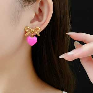 Gros plan de boucles d'oreilles nœud doré avec cœurs roses portées par un mannequin