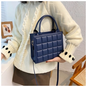 Detail of dark blue quilted square handbag worn by model against neutral background