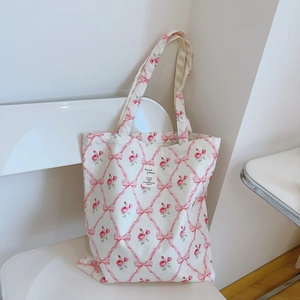 Detail of white cotton tote bag featuring pink floral ribbon pattern and stitched label