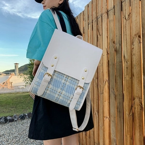 Detail of white leather and blue plaid tweed backpack with gold buckles in outdoor light