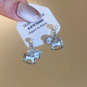 Detail of silver rocking horse earrings with sparkling zircons and a white pearl accent