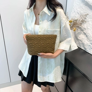 Brown quilted minimalist clutch bag held by model featuring floral texture and simple design