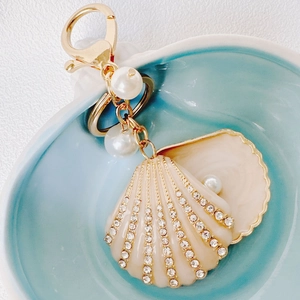 Detail of seashell keychain with enamel finish, pearls and rhinestones on blue plate