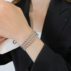 Detailed view of triple-layered silver beaded bracelet worn on a wrist against black fabric