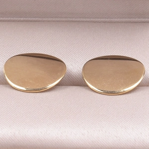 Macro shot of polished gold irregular bean earrings presented in a luxury satin jewelry box