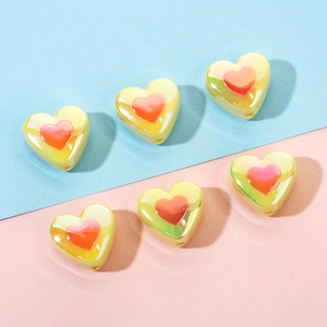 Close-up of yellow and orange heart beads for DIY crafts on a blue and pink background