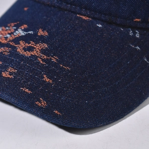 Detail of dark blue denim baseball cap brim with orange embroidery and reinforced stitching