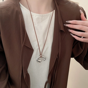 Close-up of irregular C-shaped silver pendant with brown cord on a stylish outfit