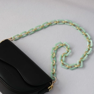 Detail of mint green acrylic and gold metal chain strap on a black matte leather bag