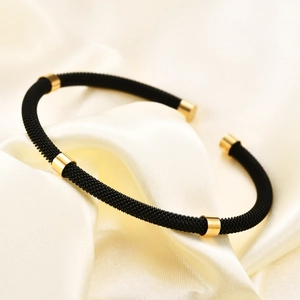Macro detail of black braided stainless steel cable bracelet with polished gold accents