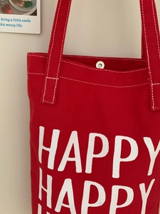Detail of red canvas tote with white topstitching, silver magnetic buckle and HAPPY print