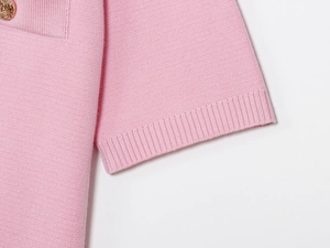 Dettaglio macro della maglia rosa a maniche corte con texture a coste e bottone d'oro