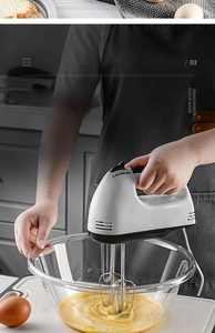 Action shot of an electric mixer stirring egg yolk inside a clear glass mixing bowl