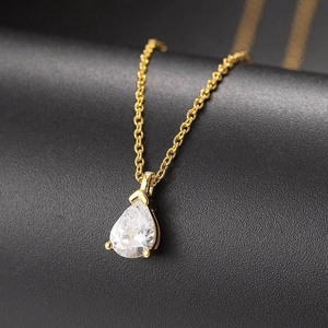 Macro view of pear shaped clear zirconia pendant on a gold chain over black leather